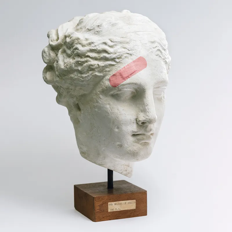 An ancient Greek head bust with a band-aid over its forehead.